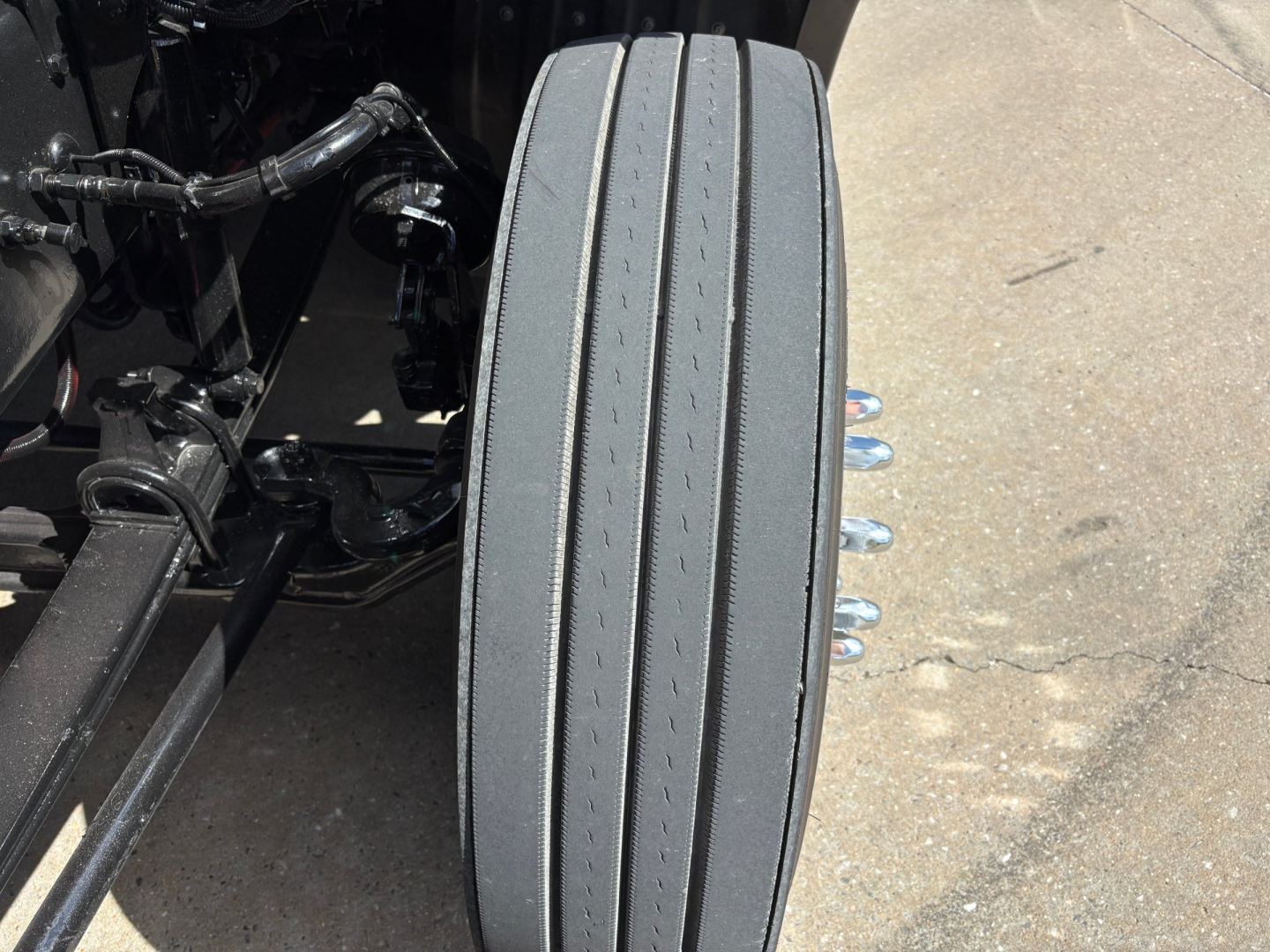 Kenworth T680 chassis with rear air suspension and a close-up of a dual-tandem drive tire along the frame; visible components include leaf springs, air lines, and wheel studs.