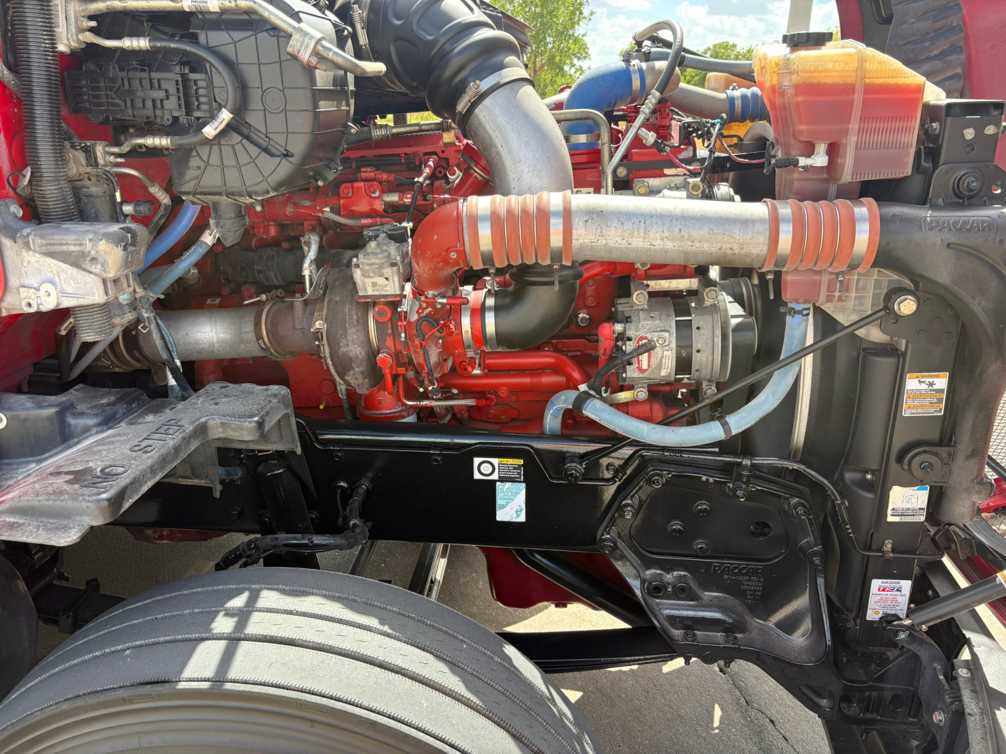 Kenworth T680 engine bay showing red engine components, hoses, reservoir, and label details visible.