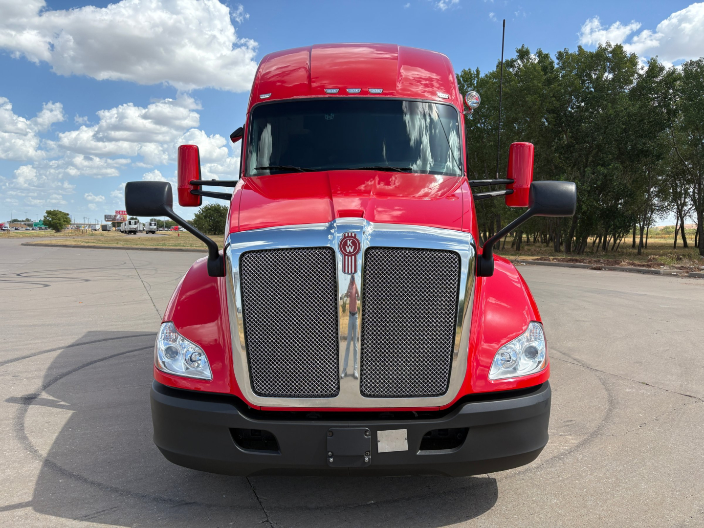Kenworth T680 truck front view showing bold chrome grille, red cab and black bumper with large mirrors.