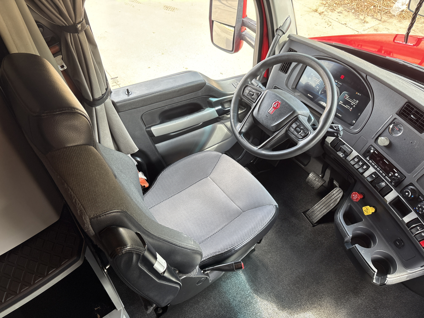 Kenworth T680 dashboard and driver seat interior showing steering wheel and instrument cluster.