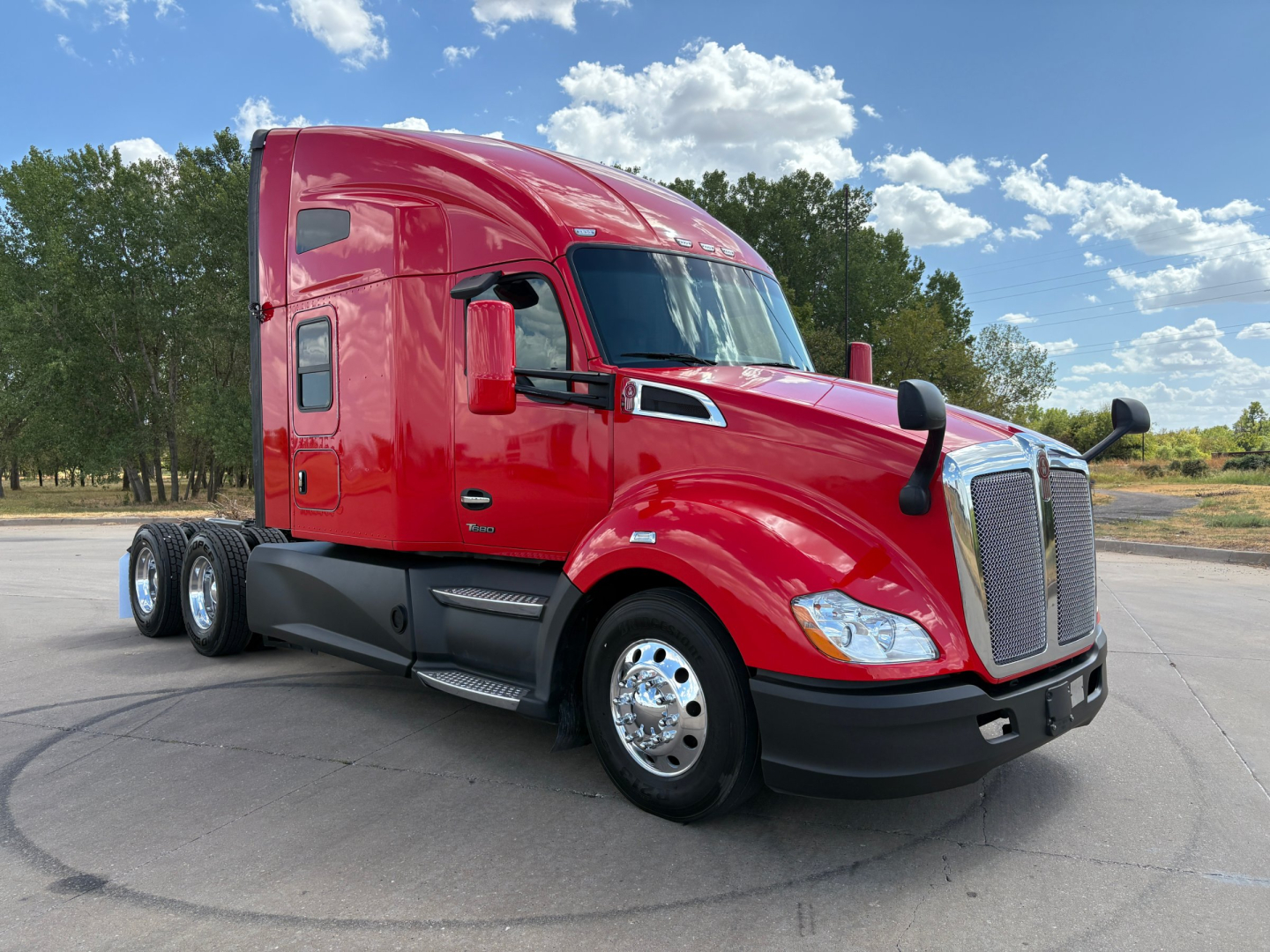 Kenworth T680 conventional sleeper truck in red, front three-quarter view showing chrome front grille, dual rear axles, and side mirrors.