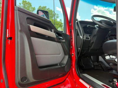 Truck cab interior door panel and steering wheel area of a red 2022 Kenworth T680, open driver door showing dashboard and floor space.