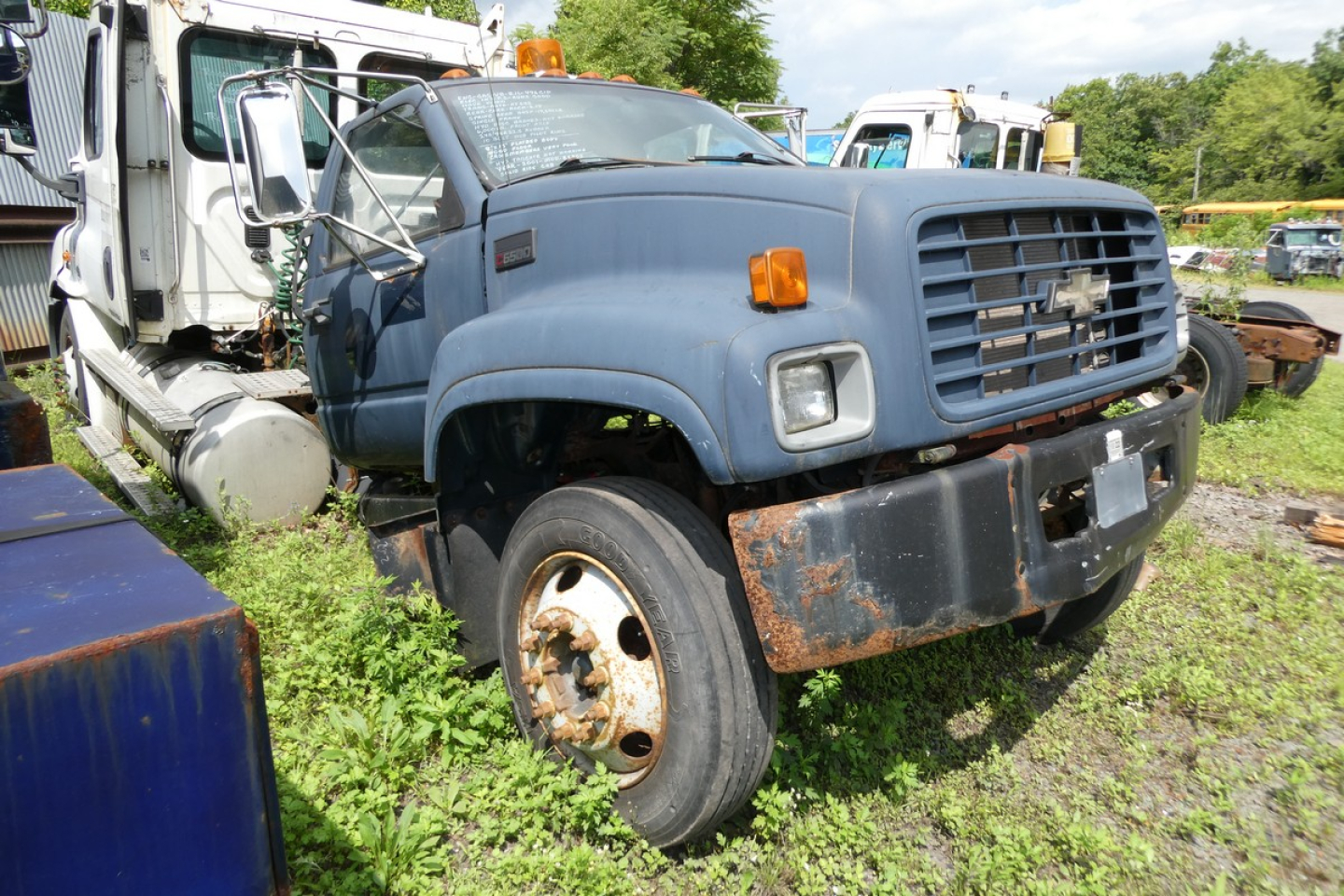 Front-left view of a blue 2001 Chevrolet C6500 cab and chassis truck with a large front grille, exposed bumper, and visible rust on the front fender and wheel area.