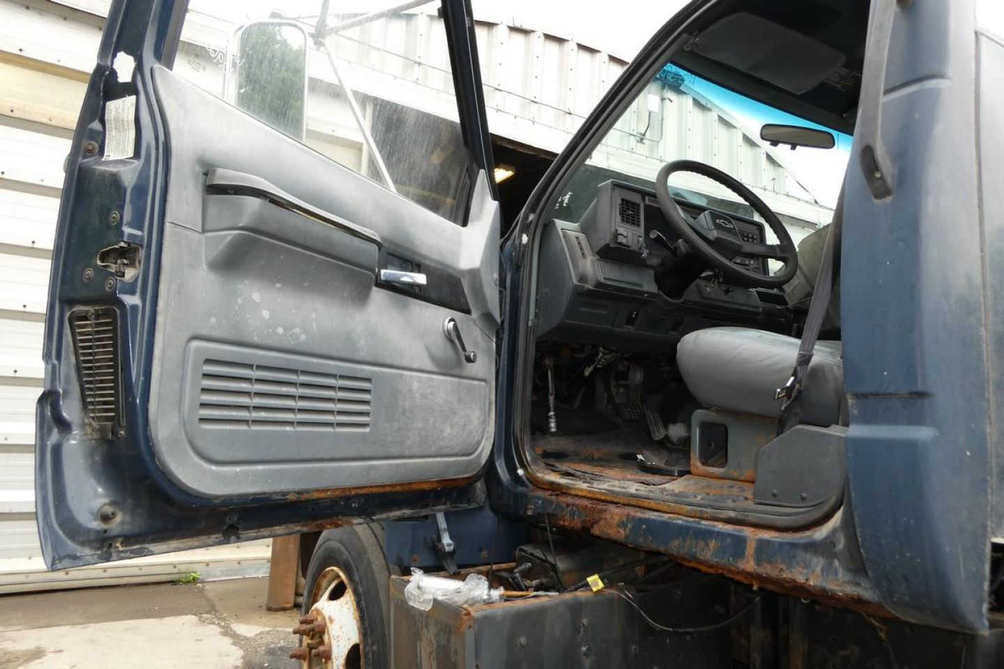 Truck cab interior view showing driver door open, steering wheel, dashboard, and entry area of a Chevrolet C6500 cab and chassis.
