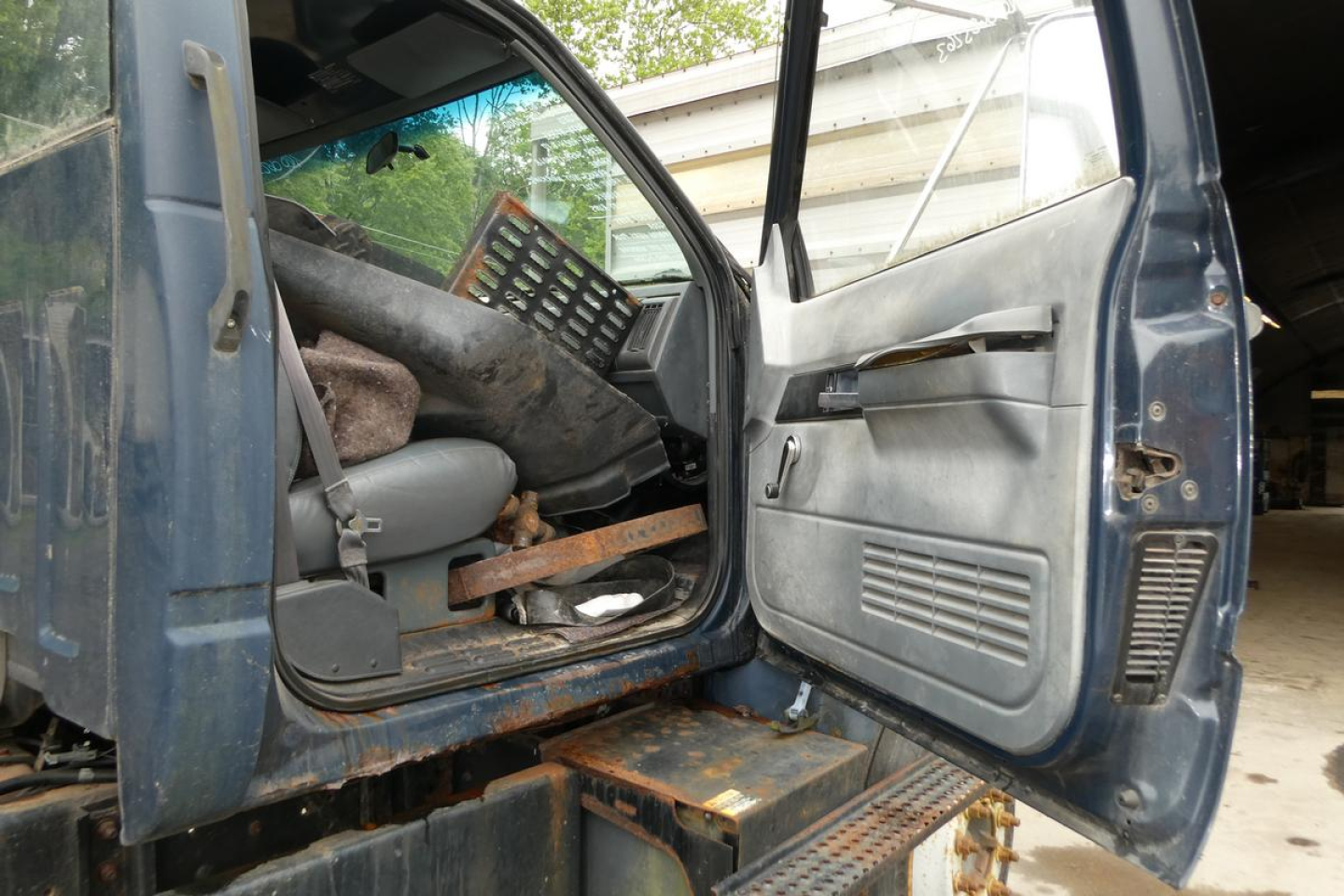 Truck cab interior view of a 2001 Chevrolet C6500 with open driver door, showing worn footwell, steering wheel, and metal steps; rust and dirt on door sill.