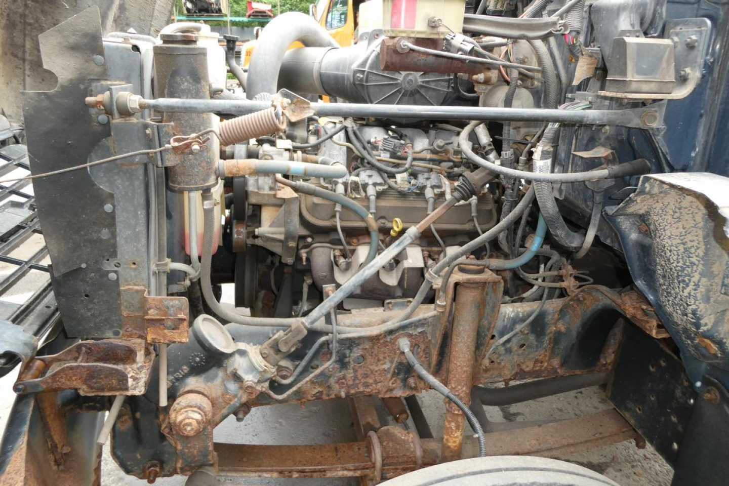 Chevrolet C6500 cab and chassis engine bay showing exposed diesel engine and surrounding components with rusted frame and hoses.
