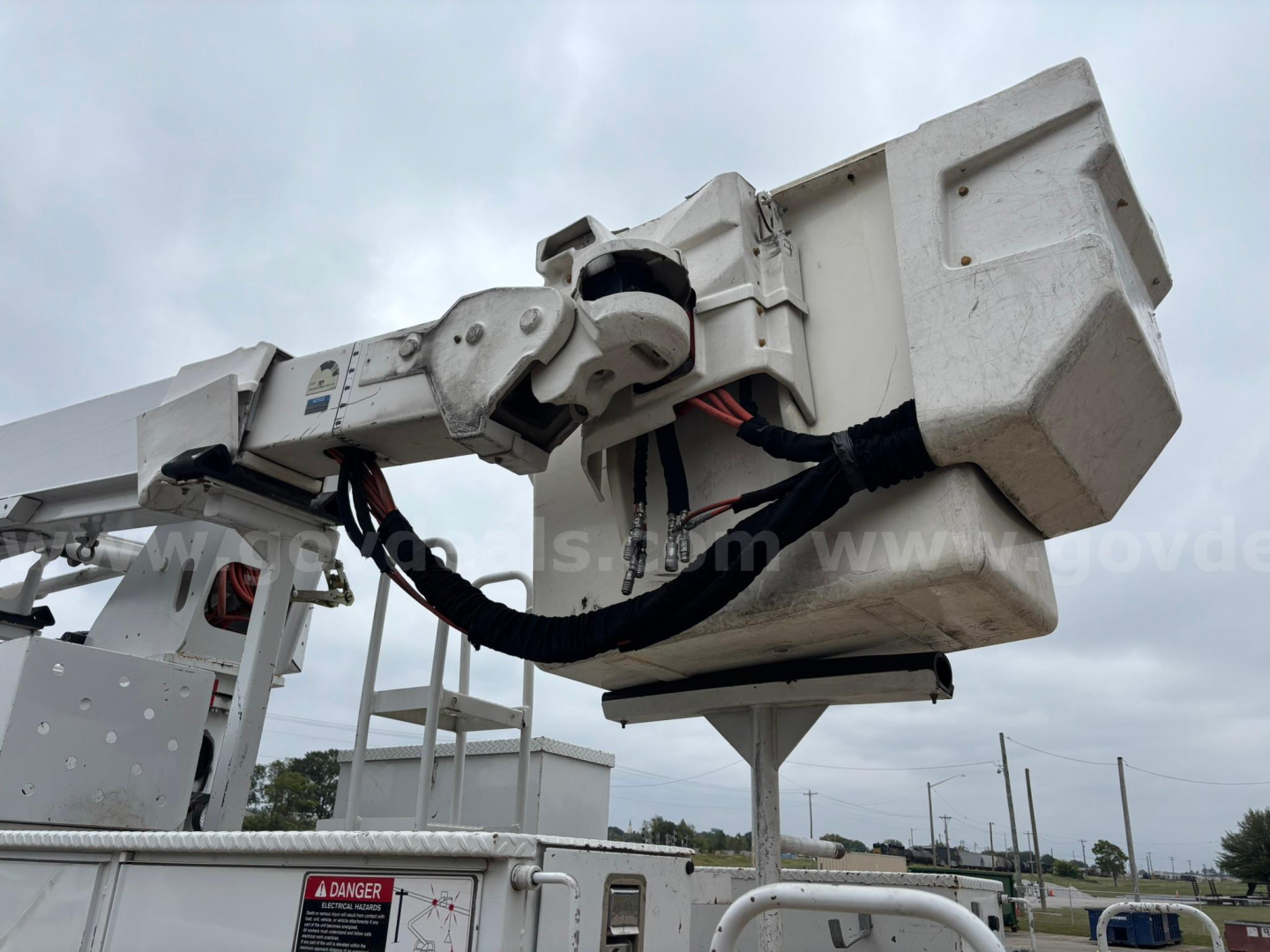 Platform bucket truck elevated boom basket with hydraulic hoses and control box mounted on boom – front view.