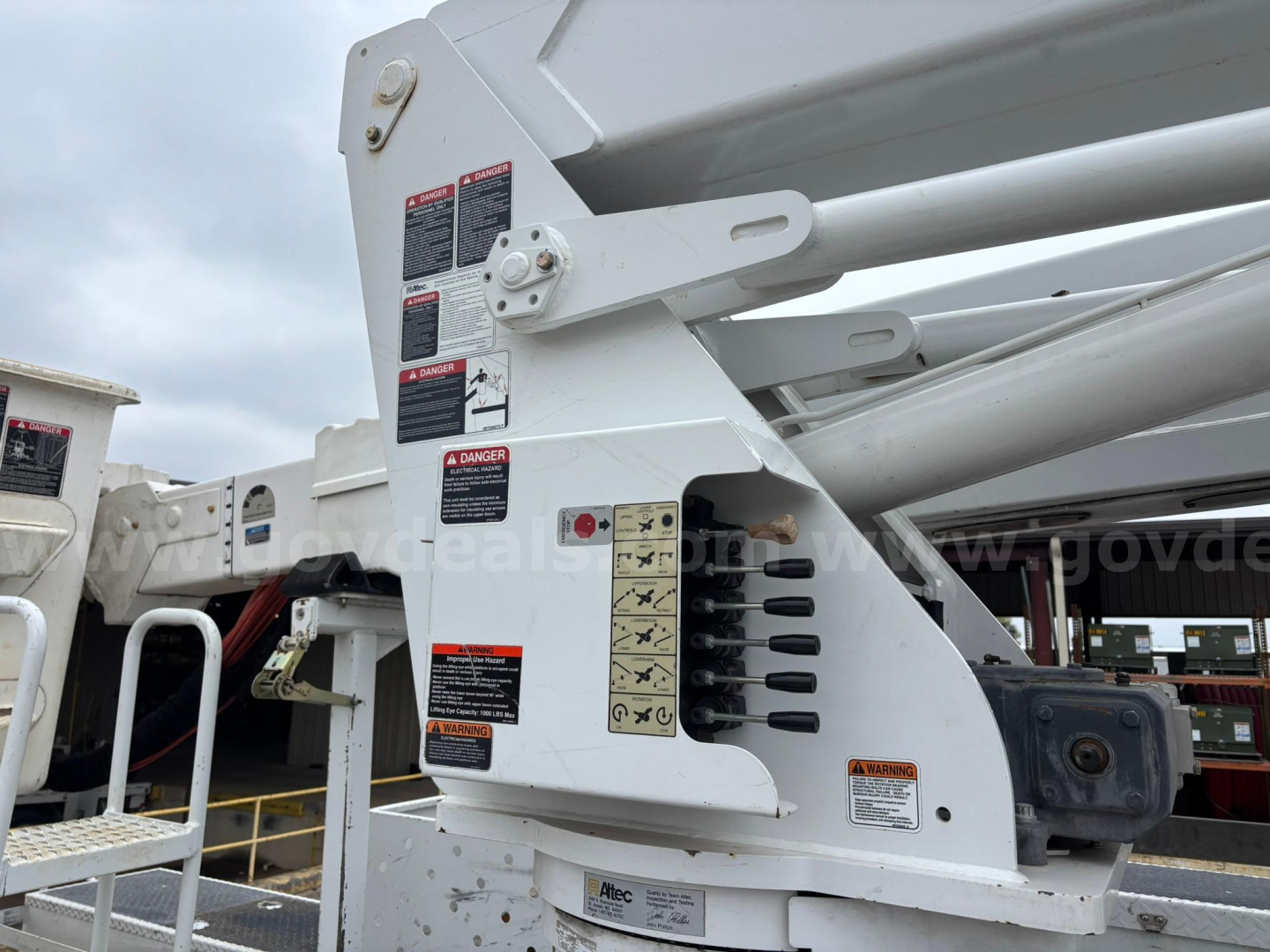 Machine-mounted controls and warning labels on a Freightliner M2 106 bucket truck boom arm, close-up side view showing hydraulic components and warning placards.