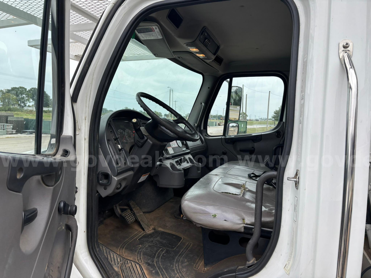 Truck cab interior of a 2014 Freightliner M2 106 bucket truck showing steering wheel, dashboard, driver seat and passenger seat.