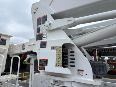 Machine-mounted controls and warning labels on a Freightliner M2 106 bucket truck boom arm, close-up side view showing hydraulic components and warning placards.