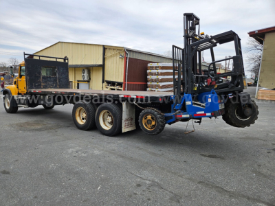 2005 Mack CV713 Granite flatbed truck with forklift attachment on the trailer showing cargo and equipment.
