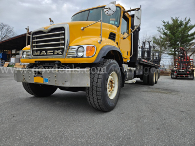 Mack CV713 Granite truck in yellow with flatbed, front view showing grille and bumper, large tires, and side mirrors.