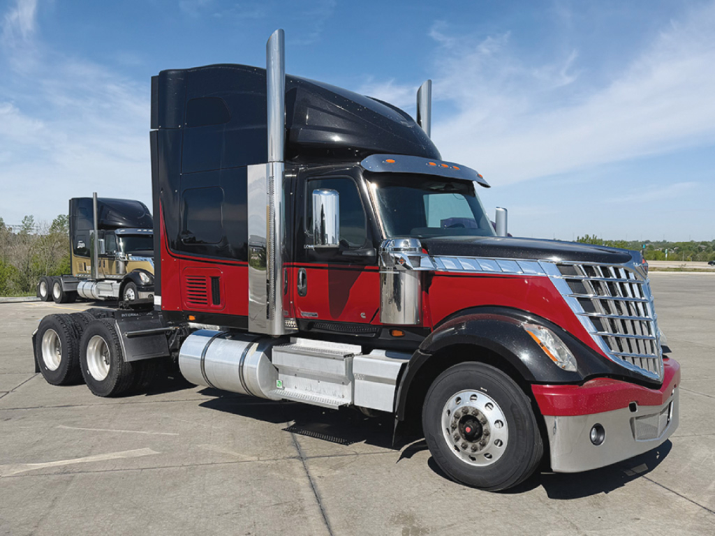 Truck cab side view of a 2021 International LoneStar with black and red two-tone paint and chrome accents, aerodynamic mirrors, and a dual rear axle trailer chassis.