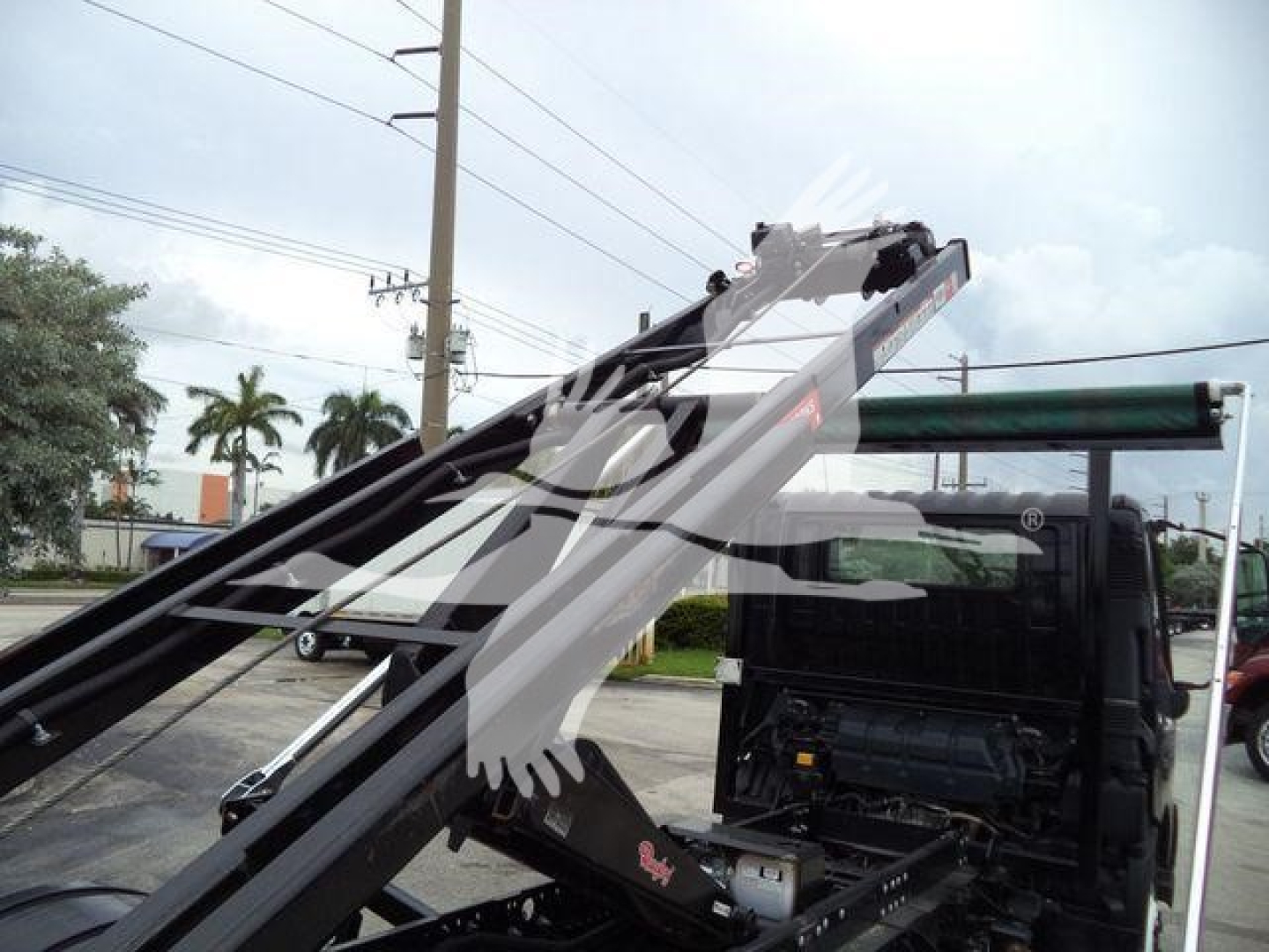 Truck cab and hydraulic arm of a roll-off truck with a watermark overlay; visible components include the truck chassis and lifting arms.