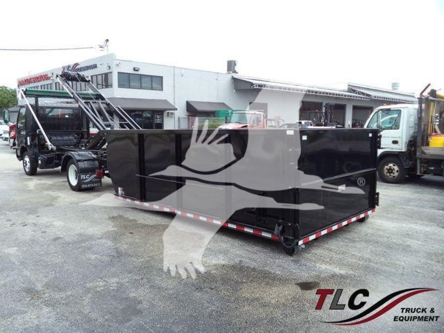 Truck with black roll-off container in yard showing Hino 195 bumper and nearby equipment.