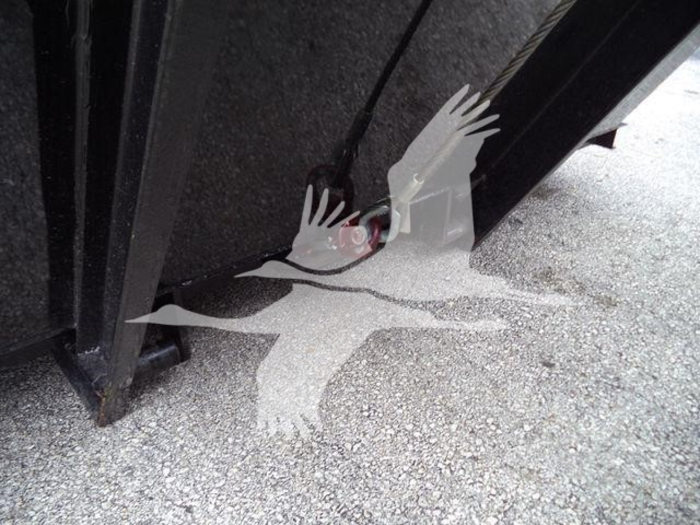 Truck chassis or undercarriage area showing a hydraulic line and component near the frame, with a partial wheel and asphalt surface.