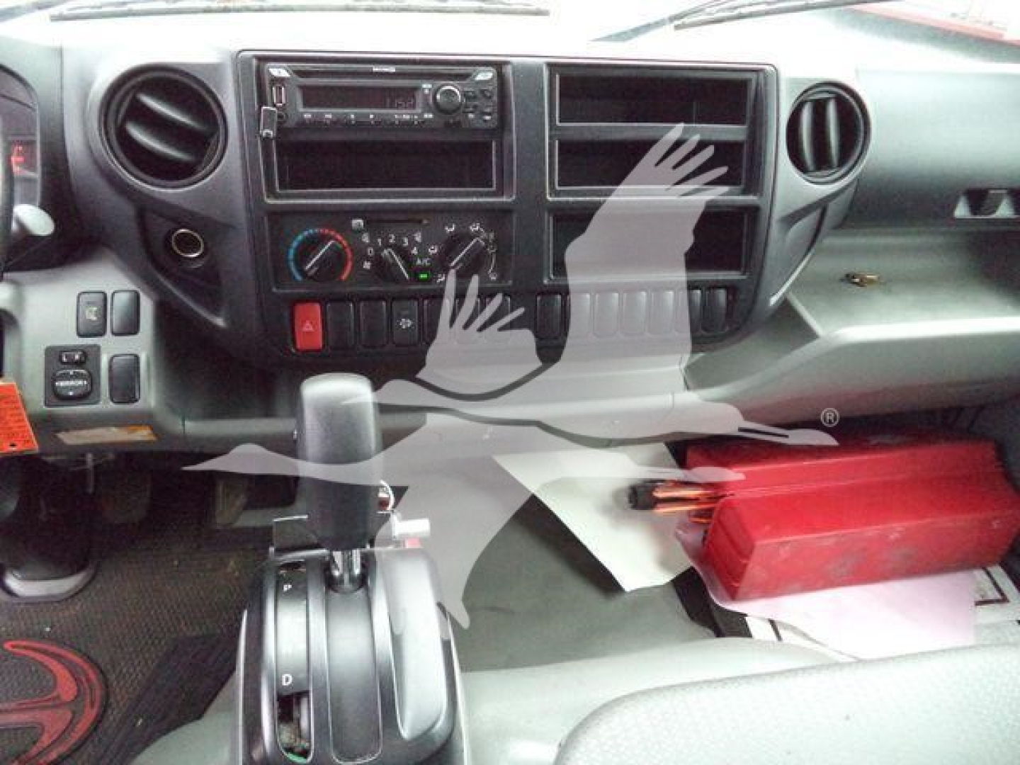 Hino 195 interior dashboard with steering column, center console, CD player, HVAC controls, and a red tool/storage box on passenger floor.