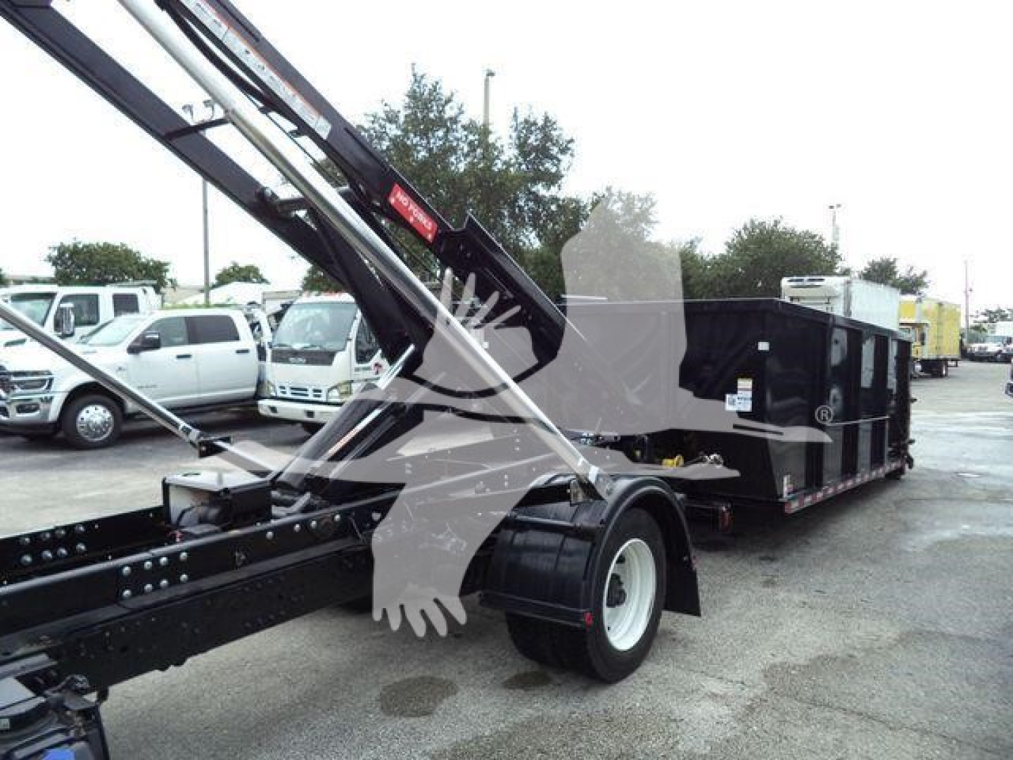 Hino 195 roll-off truck with long dump body and crane arm visible, front view of wheel and chassis.