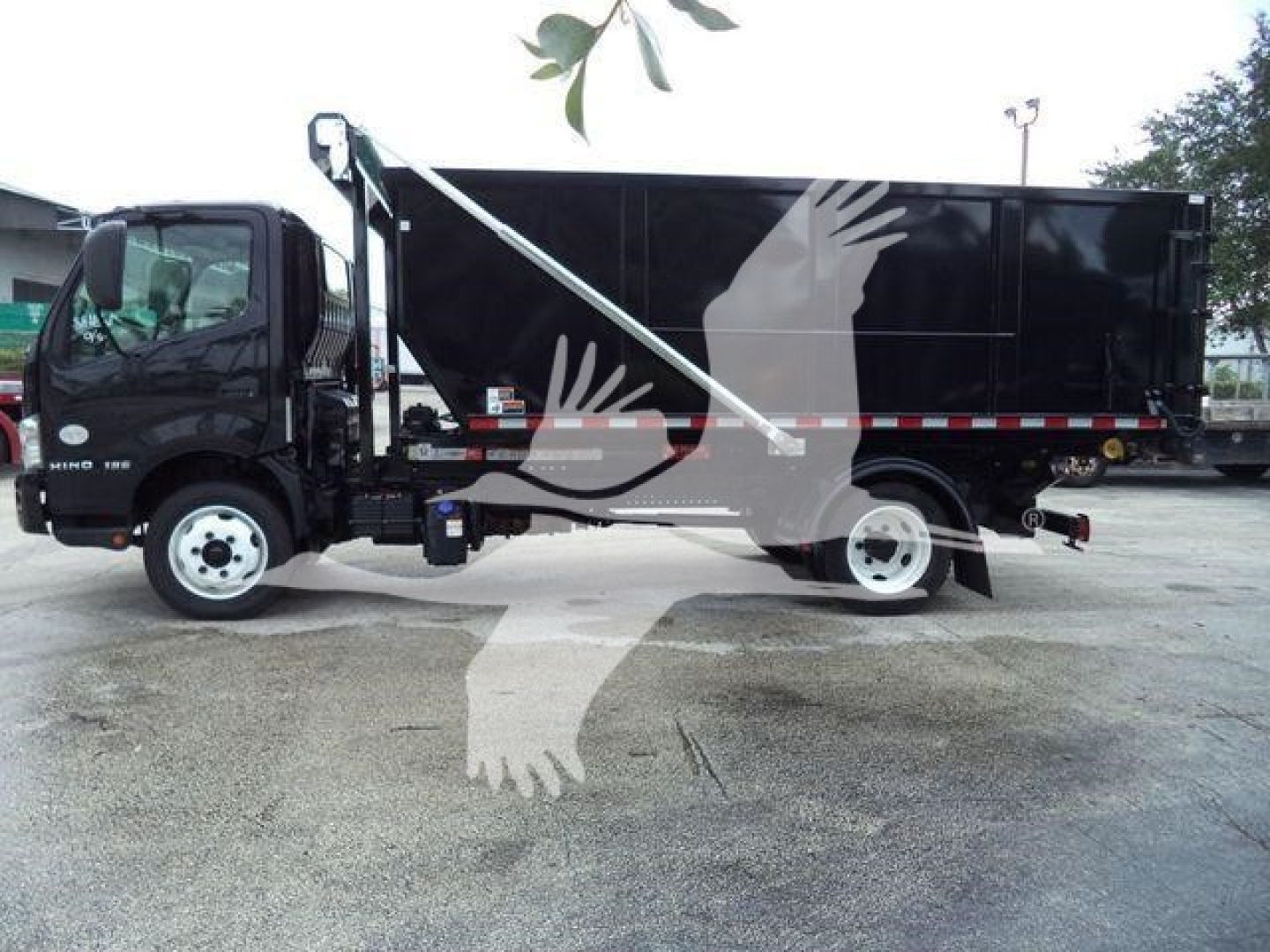 Truck side view showing a black Hino roll-off body with white cab and hydraulic boom, side steps, and roll-off container.