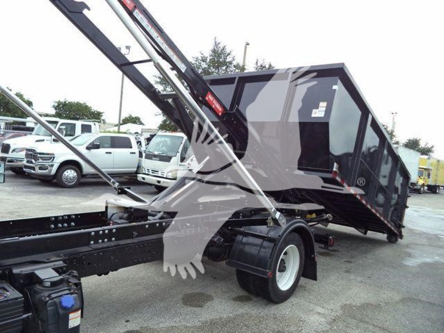 Truck chassis and tipped roll-off container with hydraulic crane arms visible; no legible text visible on components.