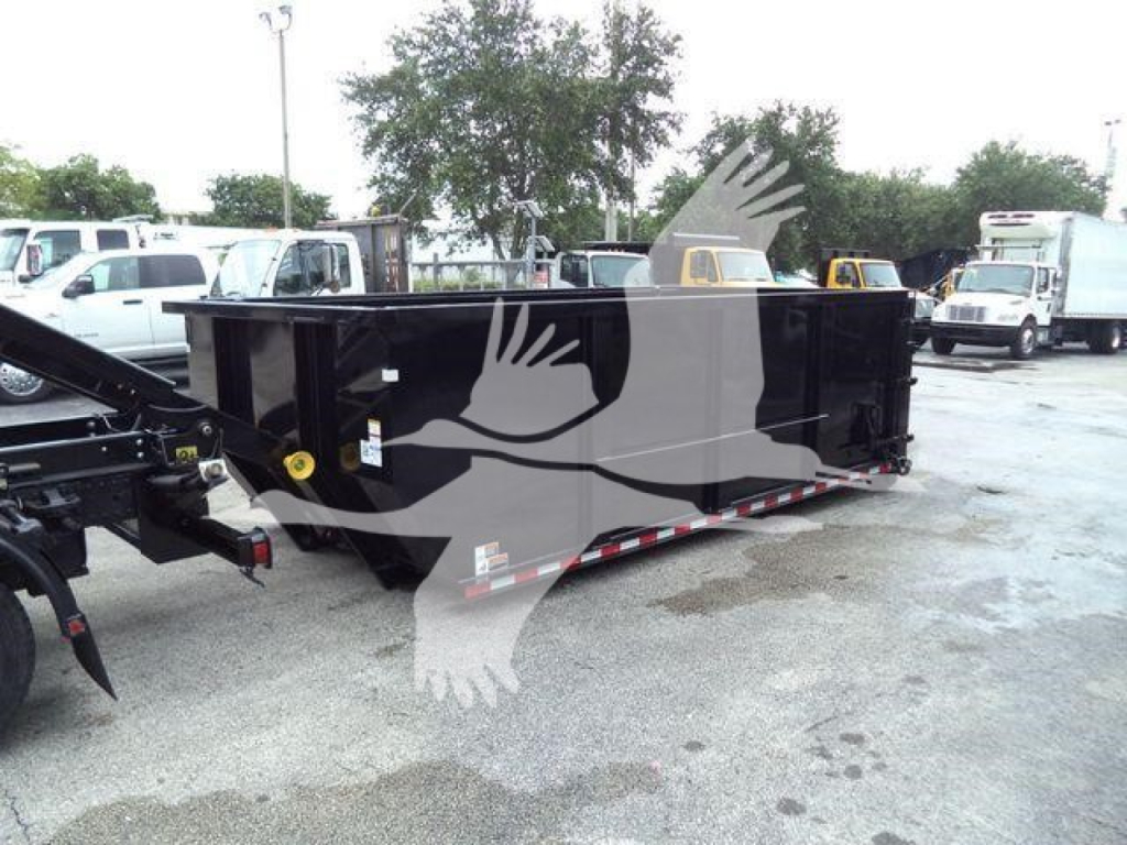 Rolloff truck bed attached to a trailer in a lot, showing a large black dump box with safety decals and chains.