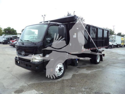 Truck in-servicing area showing 2019 Hino 195 roll-off truck with black cab and large dumpster body attached.