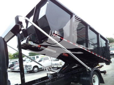 Truck bed in raised position with hydraulic cylinders; cab and reflection in side panels; surrounding vehicles in lot.