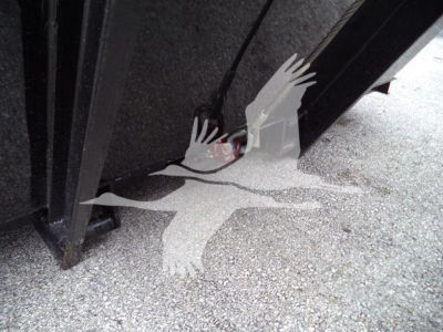 Truck chassis or undercarriage area showing a hydraulic line and component near the frame, with a partial wheel and asphalt surface.