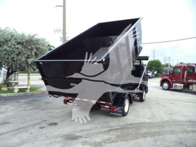 Trailer with a raised dump bed showing rear of truck and safety decals on mudflap. Text on tires and bumper not legible.