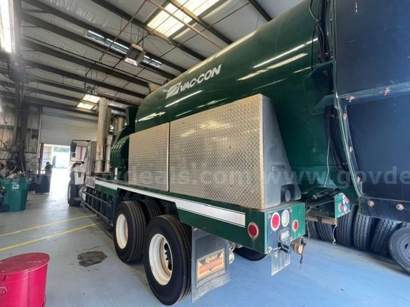 Vacuum truck (2019 International WorkStar 7500) rear-side view showing green tank with diamond plate toolbox, dual rear axles, and Waste Management style rear bumper.