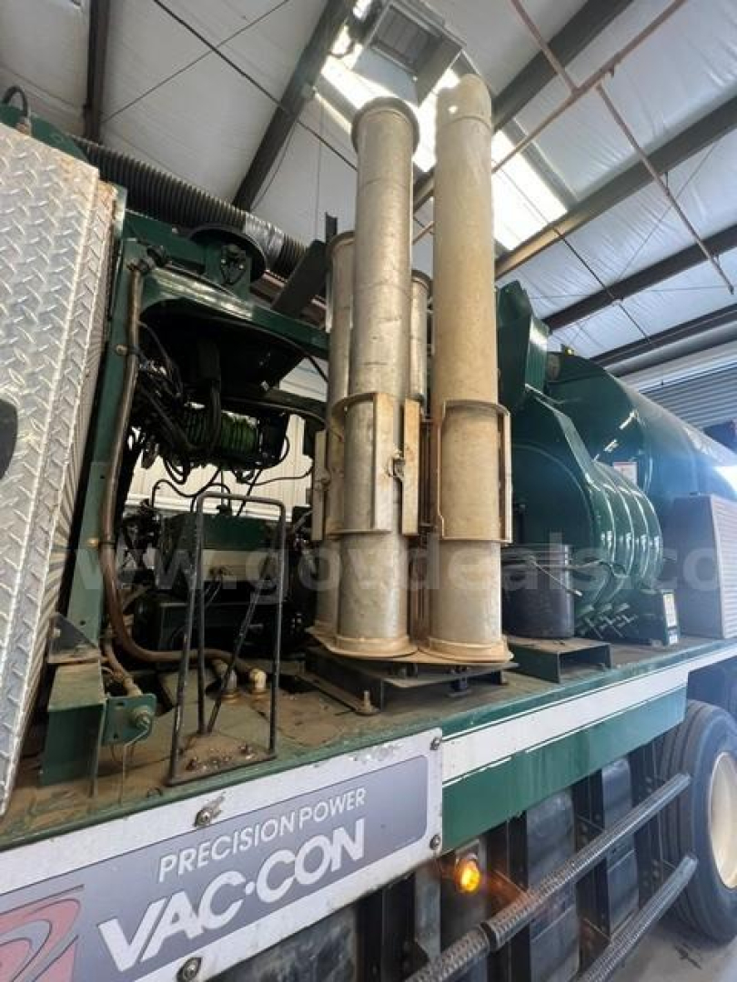 Vacuum truck engine bay with two tall exhaust stacks and green equipment on a flatbed; visible labels include PRECISION POWER VAC-CON on the side.