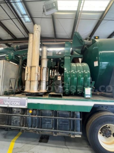International WorkStar 7500 truck engine bay showing large green compressor/tank assembly and exhaust stack on a flatbed trailer within a shop.