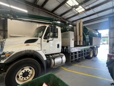 International WorkStar 7500 vacuum truck showing white cab and green vacuum tank with hoses in a shop bay.