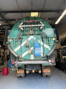 Back view of green International WorkStar 7500 vacuum truck with rear equipment and hoses, tank cap, and reflective chevron pattern.