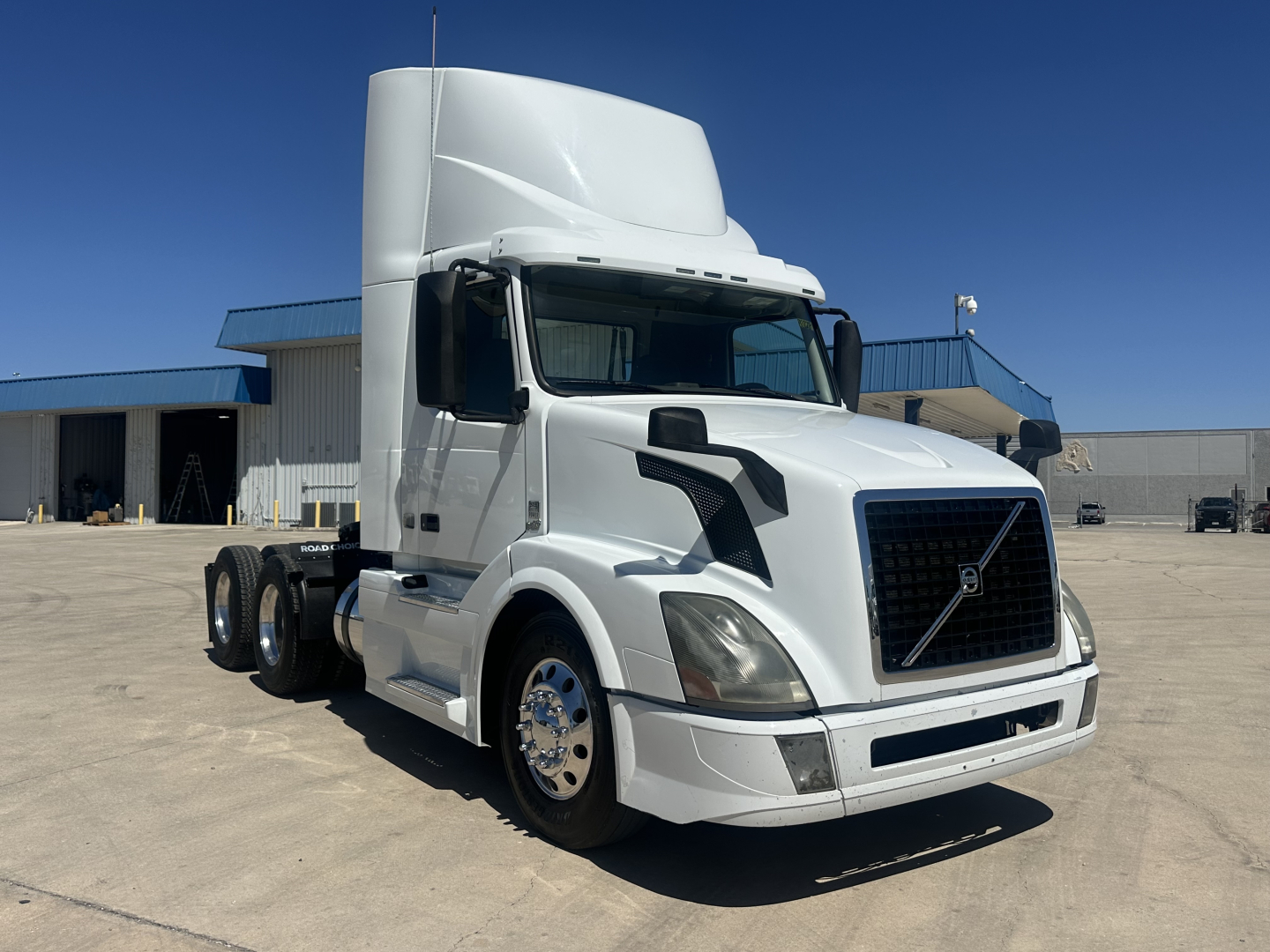 Volvo VNL64T300 daycab tractor in white parked on lot, side view showing cab, hood, grille with Volvo emblem, front bumper, mirrors, and chrome wheels.