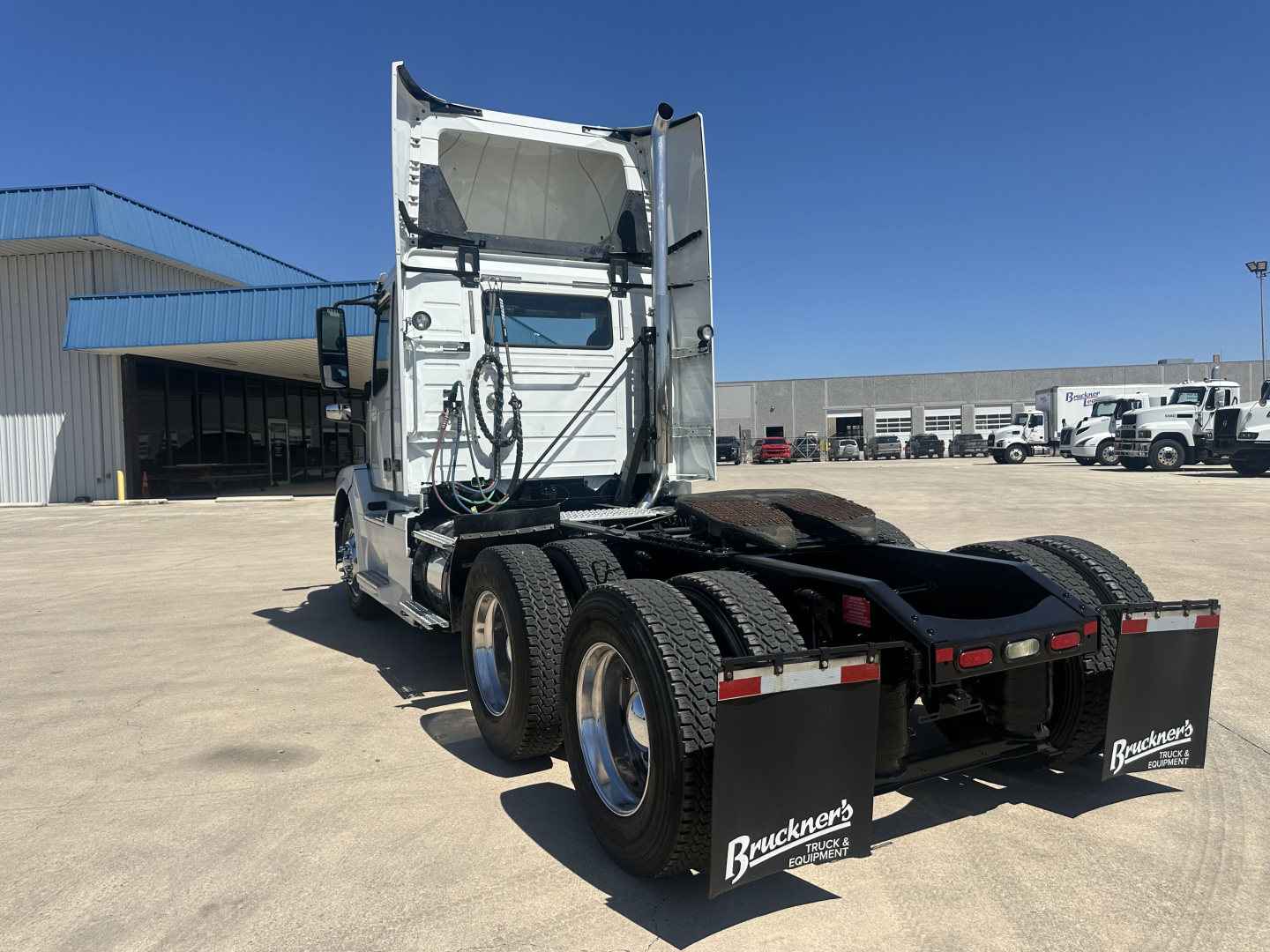 Volvo VNL64T300 tractor rear view showing tandem axles, fifth wheel missing, mud flaps with Bruckner’s logo, white cab, clear sky.