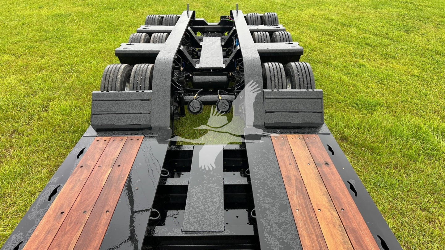 Lowboy trailer frame showing multiple axles and wooden deck sections, from rear view.