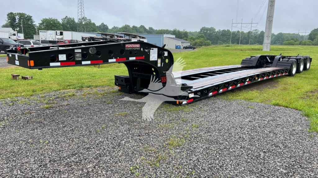 Fontaine lowboy trailer in a yard showing a long flatbed with multiple axles and safety decals.