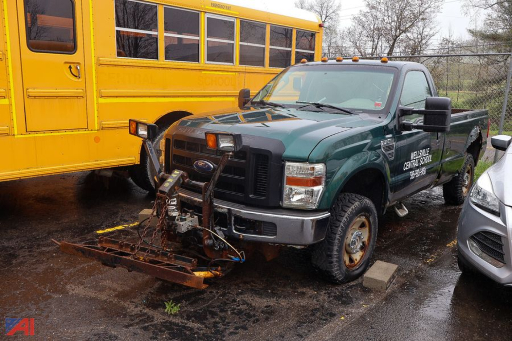 2009 Ford F250 pickup truck with plow attachment in front, green crew cab with yellow school bus in background.