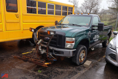 2009 Ford F250 pickup truck with plow attachment in front, green crew cab with yellow school bus in background.