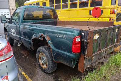 Ford F-250 pickup truck with plow and damaged rear quarter panel on the driver side in a parking lot.