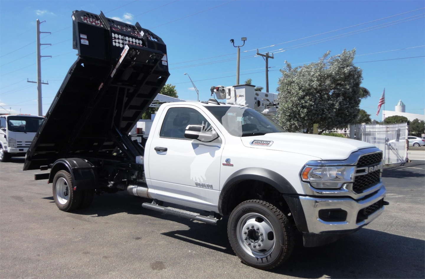 Ram 5500 HD dump truck with a black hydraulic bed tilted up in a dealership lot.
