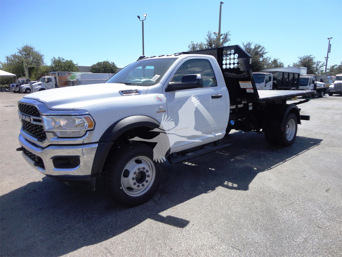 Ram 5500 HD flatbed hooklift truck in white with decorative wolf graphic on door and black toolbox, stock image showing side view.