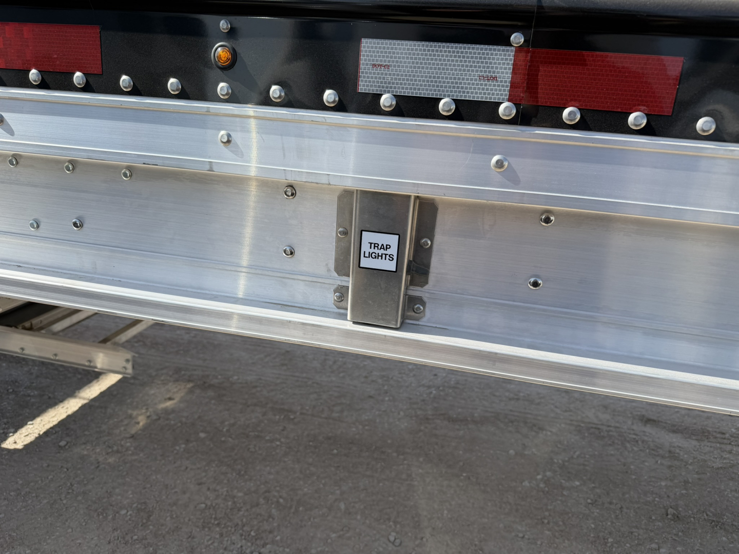 Trailer rear showing trap lights housing on aluminum grain hopper with shiny corrugated sidewalls and bumper area.