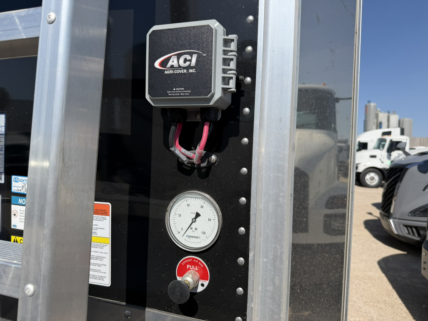 Trailer vertical control panel with ACI ABS cover box, wiring, a round gauge, and a red knob on a black panel, with a partial sticker and bolts along the edge.