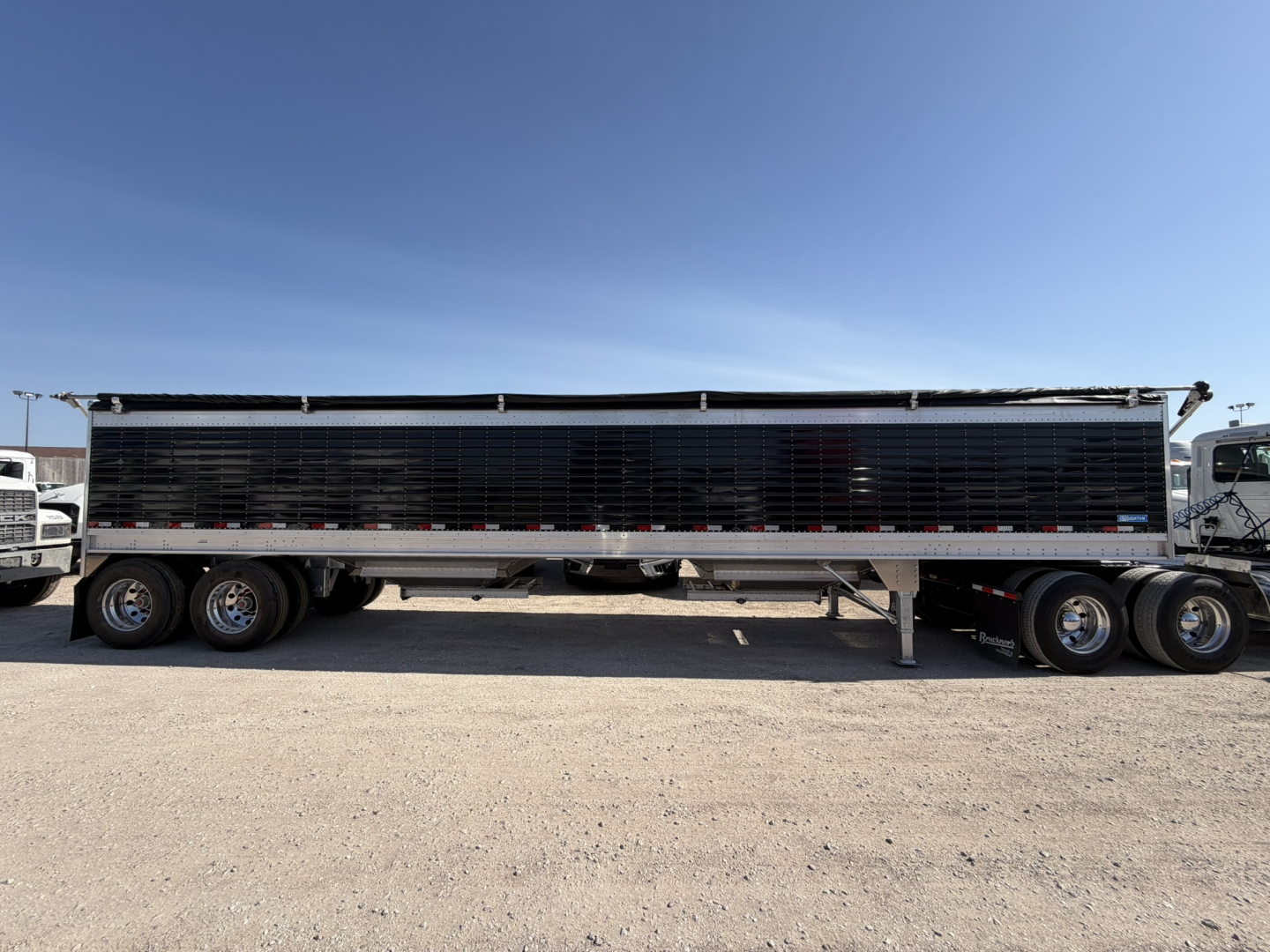 Aluminum grain hopper trailer with 68" corrugated sidewalls in a side view, black perforated panels and dual rear doors, parked on dirt lot.
