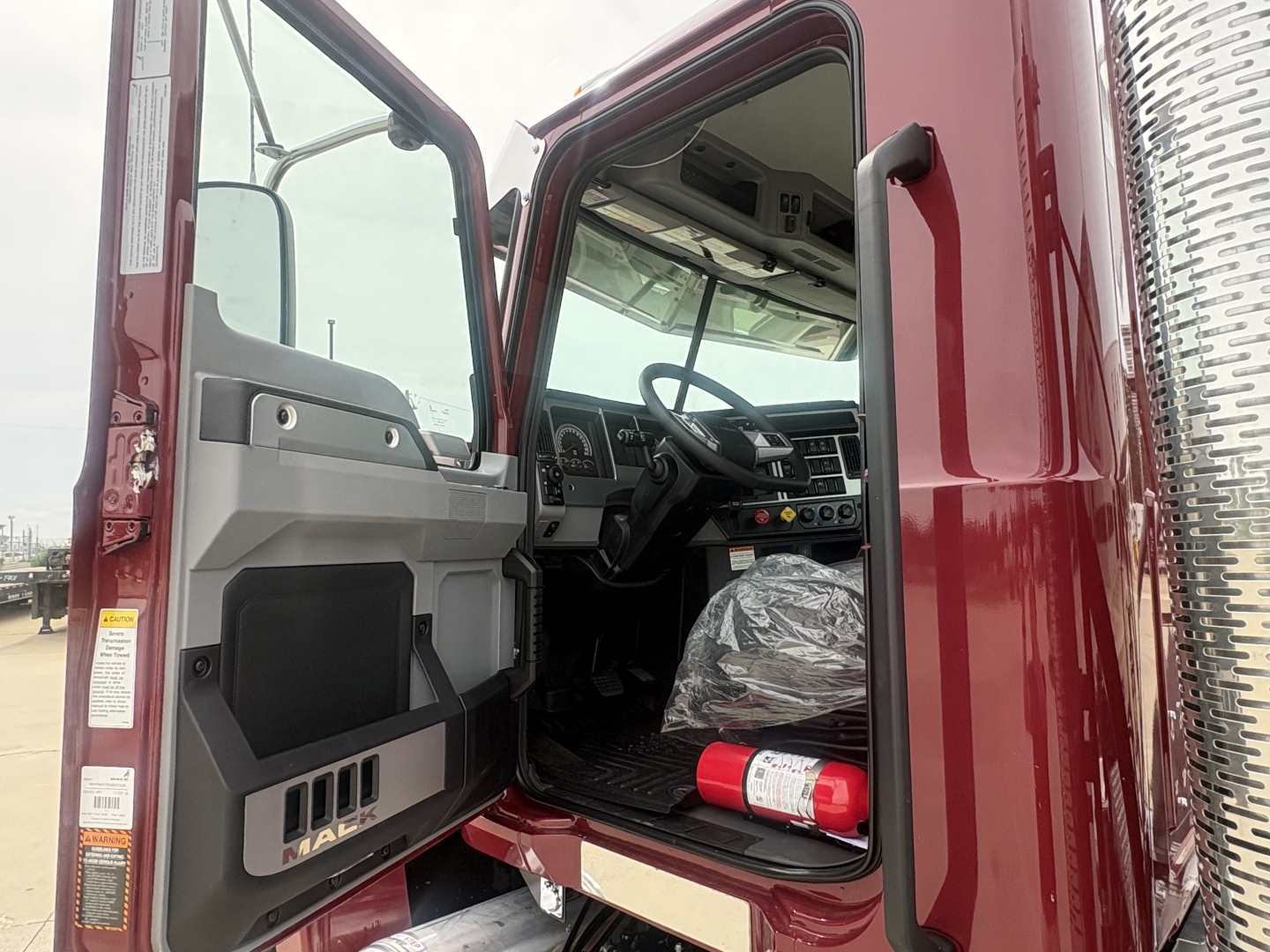 Truck cab interior showing Mack PI64T dashboard and steering wheel with exposed driver's door open.