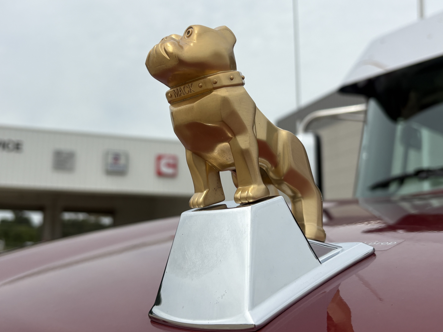 New Mack PI64T truck image showing gold bulldog hood ornament on maroon cab.