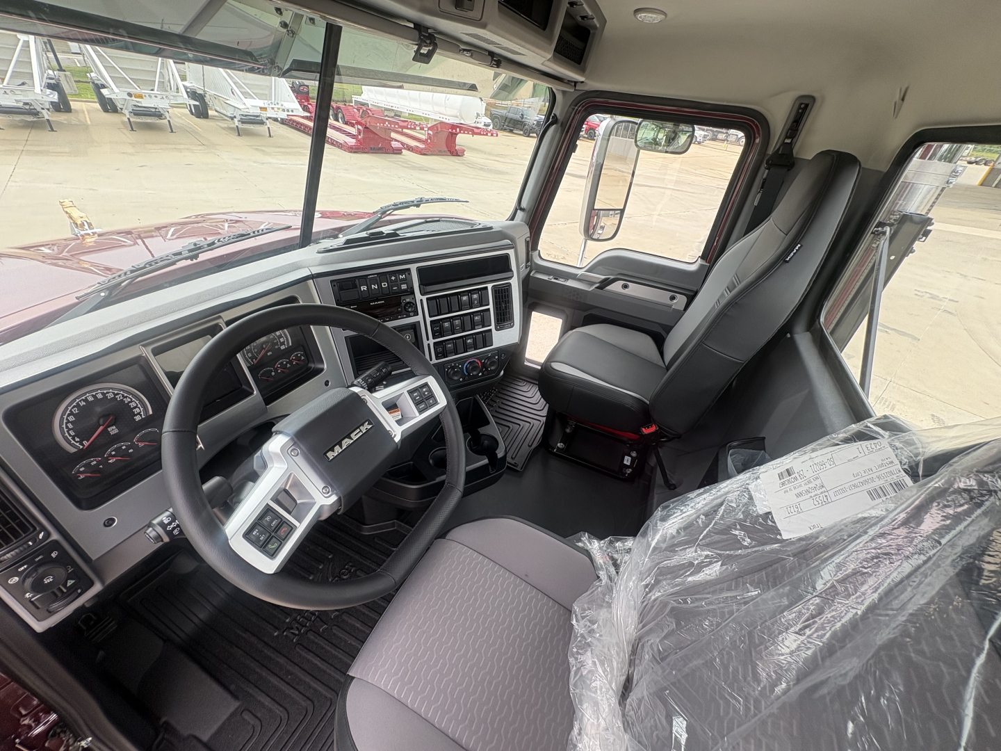 Cab interior of a new 2027 Mack PI64T truck showing steering wheel, dashboard, and front seats with plastic packaging on passenger seat.