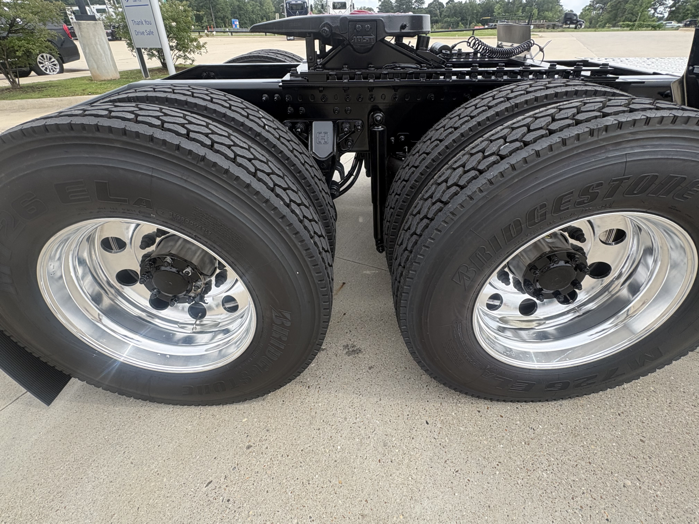 Twin rear truck axles with Bridgestone tires and polished chrome rims, chassis framing visible between wheels under a Mack PI64T tractor.